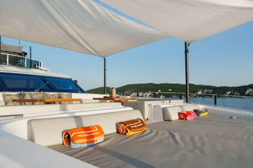 Luxurious sun loungers await on a yacht deck, offering a serene spot to enjoy the tranquil blue waters and picturesque coastline.