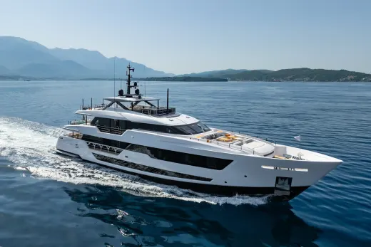 A sleek white yacht cruises through calm blue waters with distant mountains under a clear sky.