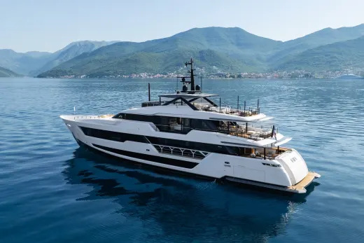 A sleek white superyacht glides through calm blue waters with lush green mountains in the background.