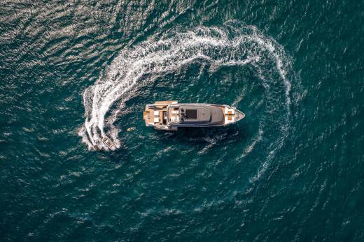 A sleek yacht glides through the turquoise ocean, leaving a swirling wake behind it.