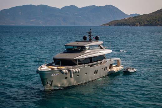 A sleek, modern yacht anchors in the azure waters off a verdant, mountainous coastline.