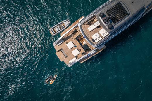 Two paddleboards and a tender float beside a luxurious yacht anchored in the clear blue sea.