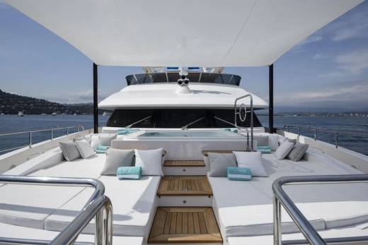 Luxurious white cushions and a steaming hot tub await relaxation on the expansive deck of this elegant yacht.