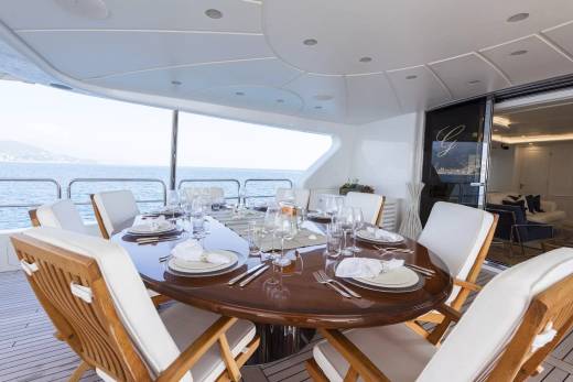 A beautifully set dining table awaits guests on a yacht's deck, offering stunning ocean views.
