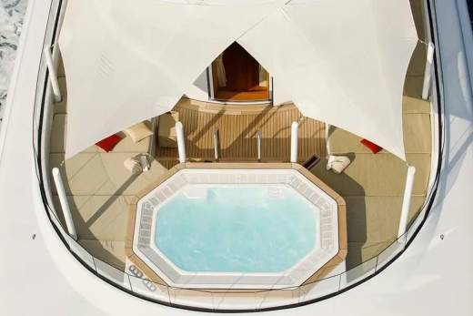 A luxurious yacht deck features a spacious hot tub surrounded by comfortable seating and shaded by elegant white canopies.