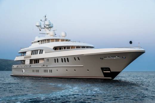 A majestic white yacht glides through calm blue waters under a serene sky.