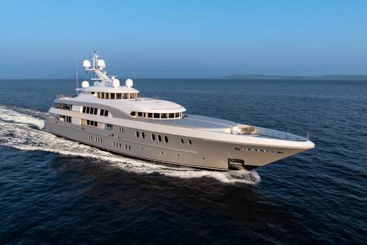 A sleek, modern superyacht glides through calm blue waters under a clear sky.