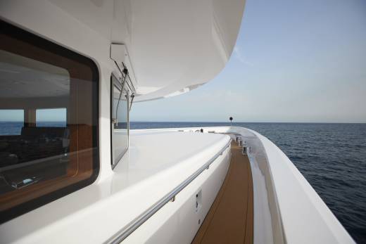 The sleek white deck of a luxury yacht curves gently towards the endless blue horizon under a clear sky.