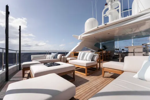 A luxurious outdoor seating area on the deck of a large yacht, with comfortable white furniture and a panoramic view of the ocean and sky in the background.