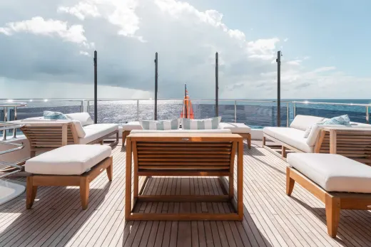 A wooden deck with comfortable outdoor furniture overlooks a vast expanse of ocean and cloudy sky.