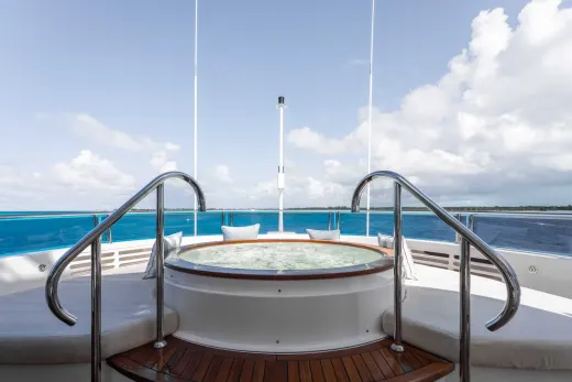 A white circular hot tub with metal railings on the deck of a boat, surrounded by a vast expanse of blue water and cloudy sky.