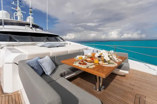 A luxurious yacht with a cozy outdoor seating area, surrounded by a stunning turquoise ocean and cloudy sky.