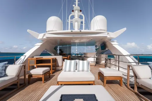 A luxurious yacht with a spacious deck featuring comfortable seating areas, surrounded by a serene blue ocean and clear sky.