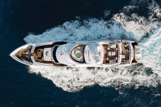 A large, luxurious yacht navigates through the choppy, dark blue waters, surrounded by a dramatic, rocky coastline.