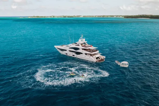 A large, luxurious yacht is anchored in the vibrant turquoise waters of a tropical paradise, surrounded by lush islands and a picturesque coastline.