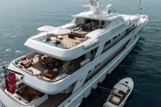 A luxurious superyacht floats serenely on the calm blue sea, its decks adorned with elegant outdoor seating and dining areas.