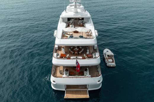 A luxurious superyacht with multiple decks and a tender boat floats serenely on the deep blue ocean.