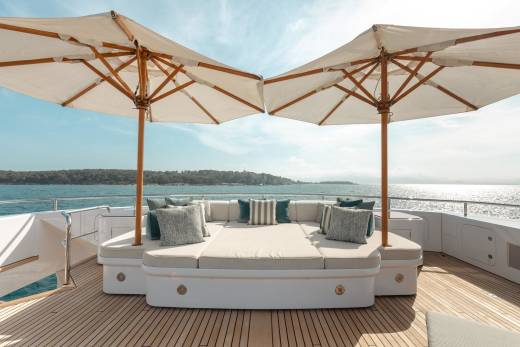 Luxurious outdoor seating on a yacht deck is shaded by two large umbrellas, offering a serene spot to enjoy the sparkling ocean view.