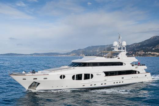A luxurious white yacht cruises through the azure waters off a picturesque coastal town nestled against rolling hills.