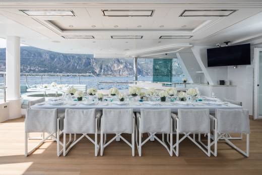 A beautifully set dining table on a yacht offers a stunning view of the Mediterranean coast.