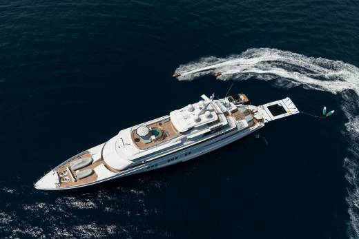 Two jet skis create white wakes as they race across the deep blue ocean near a luxurious white yacht.