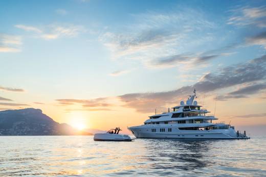A luxurious superyacht and its tender bask in the warm glow of a Mediterranean sunset.