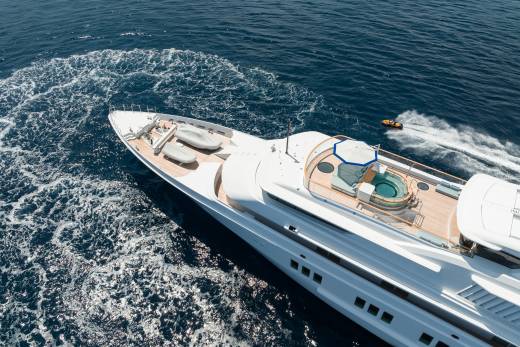 A luxurious yacht glides through the deep blue ocean, leaving a foamy wake as a jet ski speeds alongside.