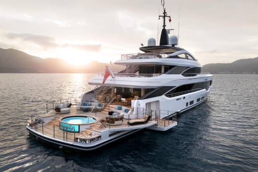 A luxurious yacht with a circular jacuzzi and plush seating enjoys a serene sunset over calm waters.