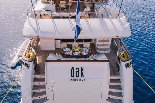 A luxurious yacht named "Oak" floats serenely on the calm blue sea, ready for an elegant dining experience.