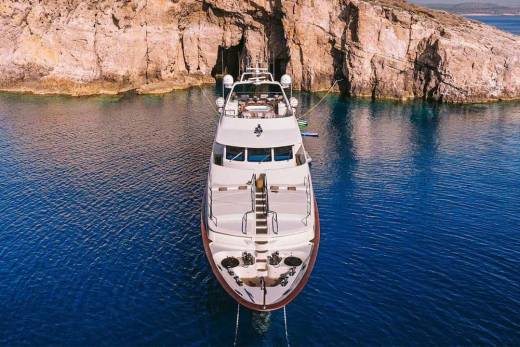 A luxurious white yacht is anchored in the crystal-clear blue waters of a secluded cove framed by rugged cliffs.