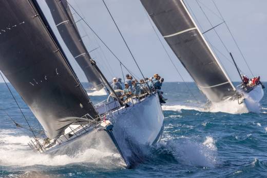Sailboats race across choppy blue waters, their dark sails billowing in the wind.