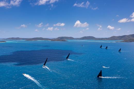 Black-sailed yachts race across the turquoise waters of the British Virgin Islands under a brilliant blue sky.