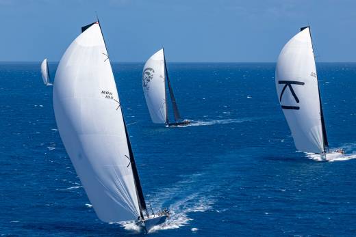Sailboats with massive white sails race across the deep blue ocean under a clear sky.