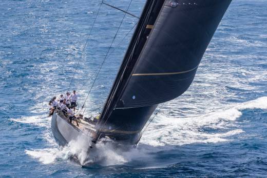 A sleek black sailboat cuts through choppy blue waters, its crew working diligently on deck.