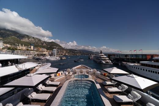 Luxury yachts fill the harbor of Monaco under a bright blue sky with fluffy white clouds.