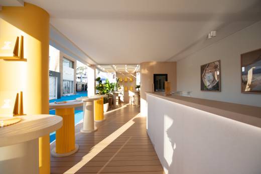 Sunlight streams across a modern outdoor lounge area featuring yellow accents and sleek furniture.