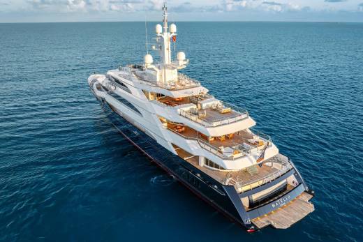 A massive, luxurious yacht sits atop the serene, azure waters, surrounded by a picturesque ocean backdrop with a cloudy sky.