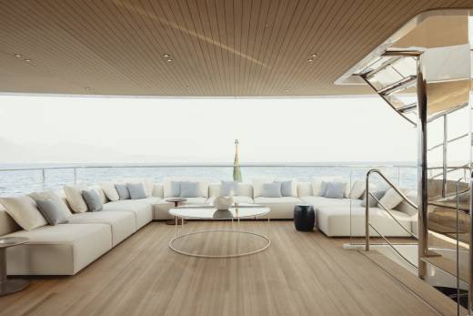 Luxurious white sectional seating and a sleek coffee table create a serene lounge area on this yacht's deck, overlooking the tranquil ocean.