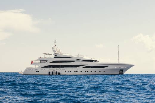 A luxurious white yacht glides across the deep blue ocean under a hazy sky.