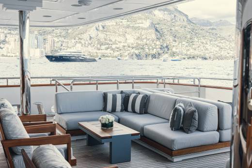 Relax on the plush outdoor seating of this luxurious yacht while admiring the stunning coastal city and mountainous backdrop.