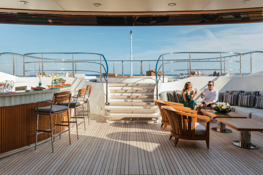 A couple enjoys drinks on the deck of a luxurious yacht, surrounded by the serene blue of the ocean.
