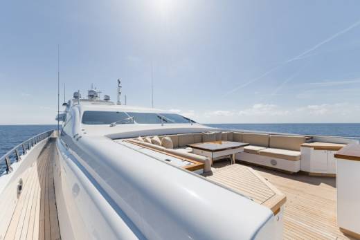 A luxurious yacht deck offers ample seating and a dining table for enjoying the serene ocean views under a clear blue sky.