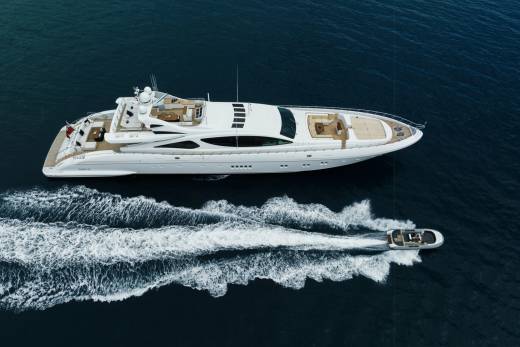 A sleek white yacht cruises through the deep blue ocean, leaving a foamy wake behind it as a smaller boat follows.