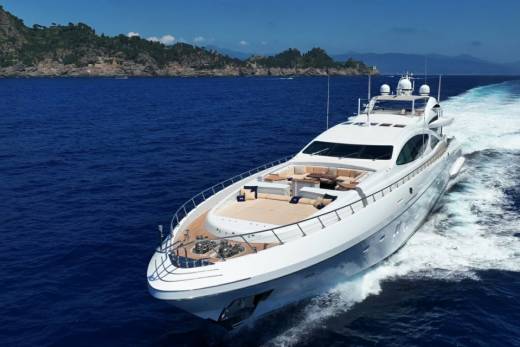 A luxurious white yacht cruises through the deep blue sea, leaving a white wake behind it.