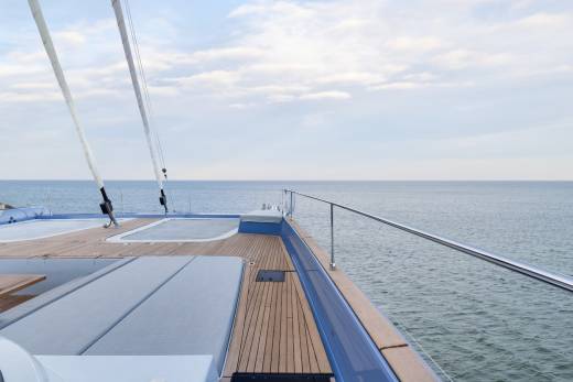 A wooden deck with railings overlooking a vast, calm ocean under a cloudy sky.