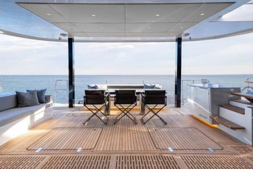 A spacious outdoor deck with a panoramic view of the ocean, featuring a seating area with chairs and a table, surrounded by a glass enclosure that provides shelter from the elements.