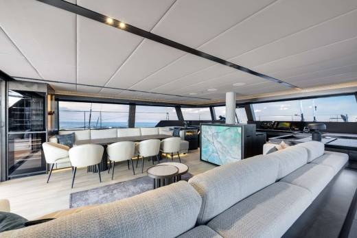A modern and spacious interior with a large sectional sofa, chairs, and a bar area overlooking a scenic view through the large windows.
