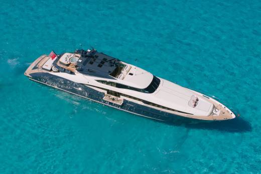 A luxurious yacht glides through crystal-clear turquoise waters under a bright sun.