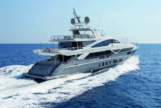 A large, luxurious yacht with multiple decks and a sleek, modern design is speeding across the calm, blue waters of the ocean against a clear sky.