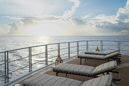 A serene ocean view with a deck featuring comfortable lounge chairs, overlooking the tranquil waters and a dramatic sky with billowing clouds.